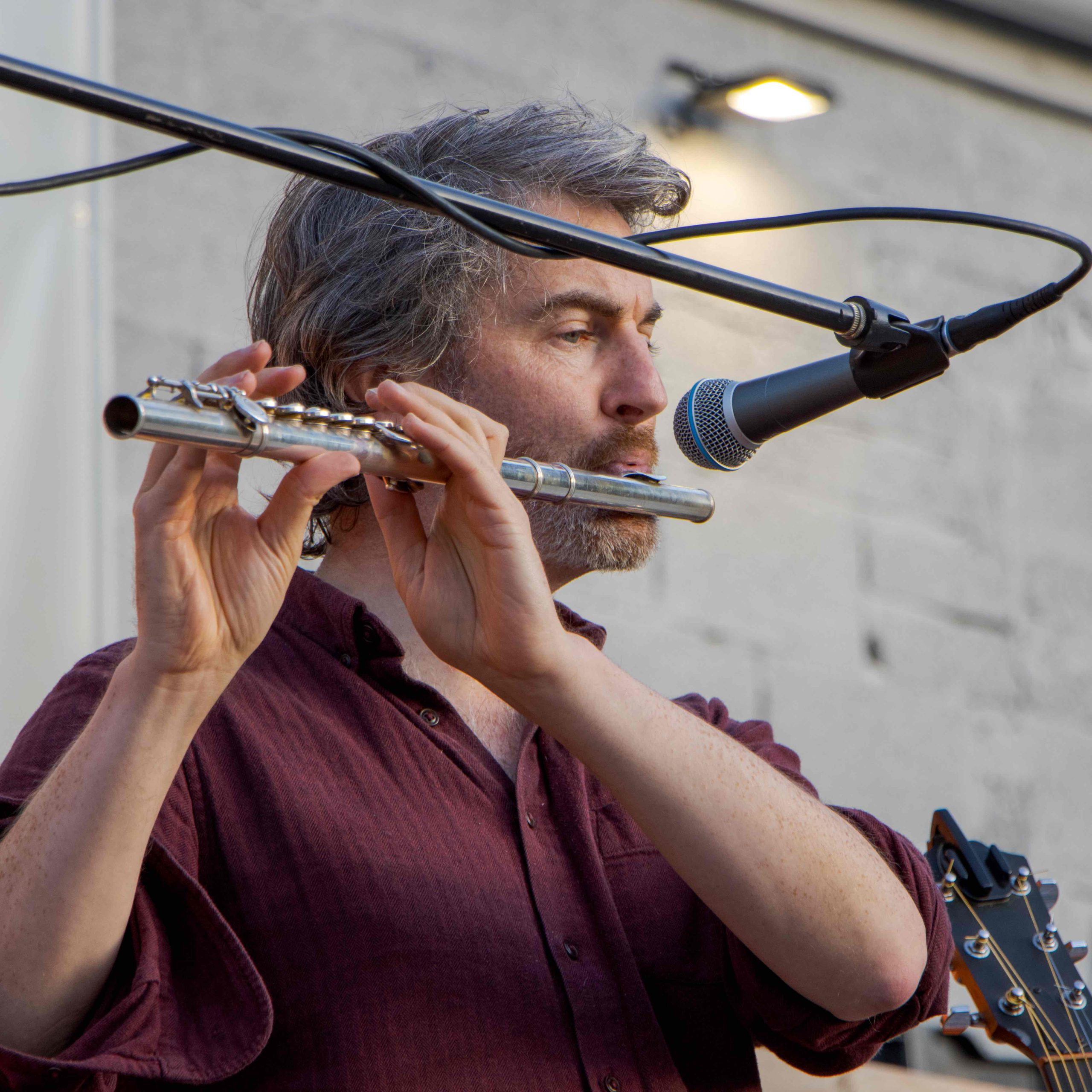 Thunderclap Murphy playing flute in natural light against a stone wall