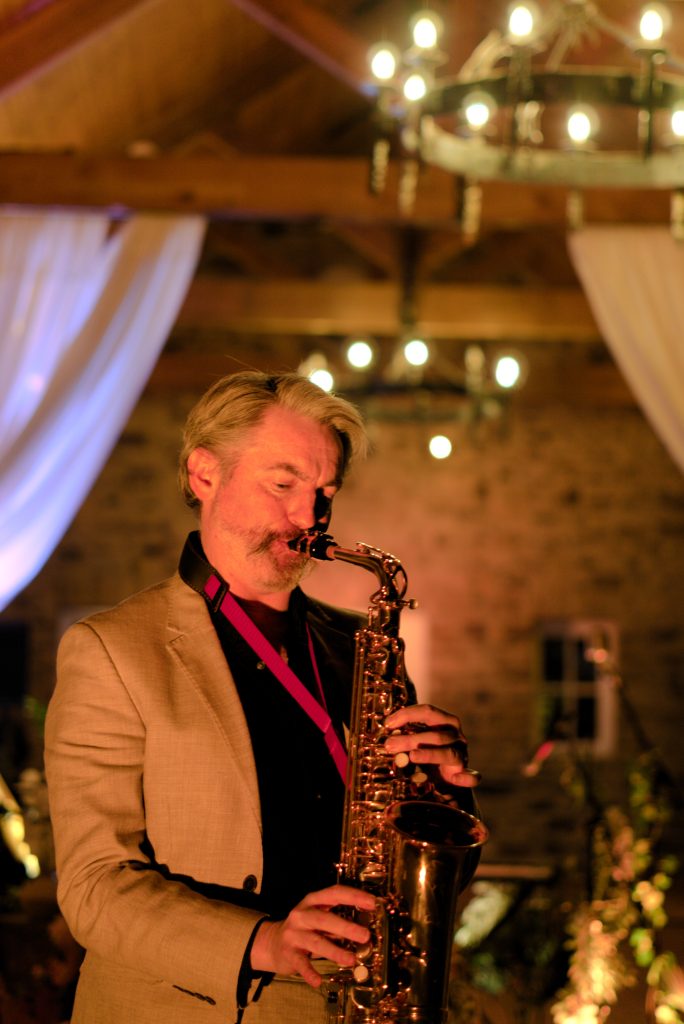 Aidan Murphy playing saxophone under a chandelier at Camelot