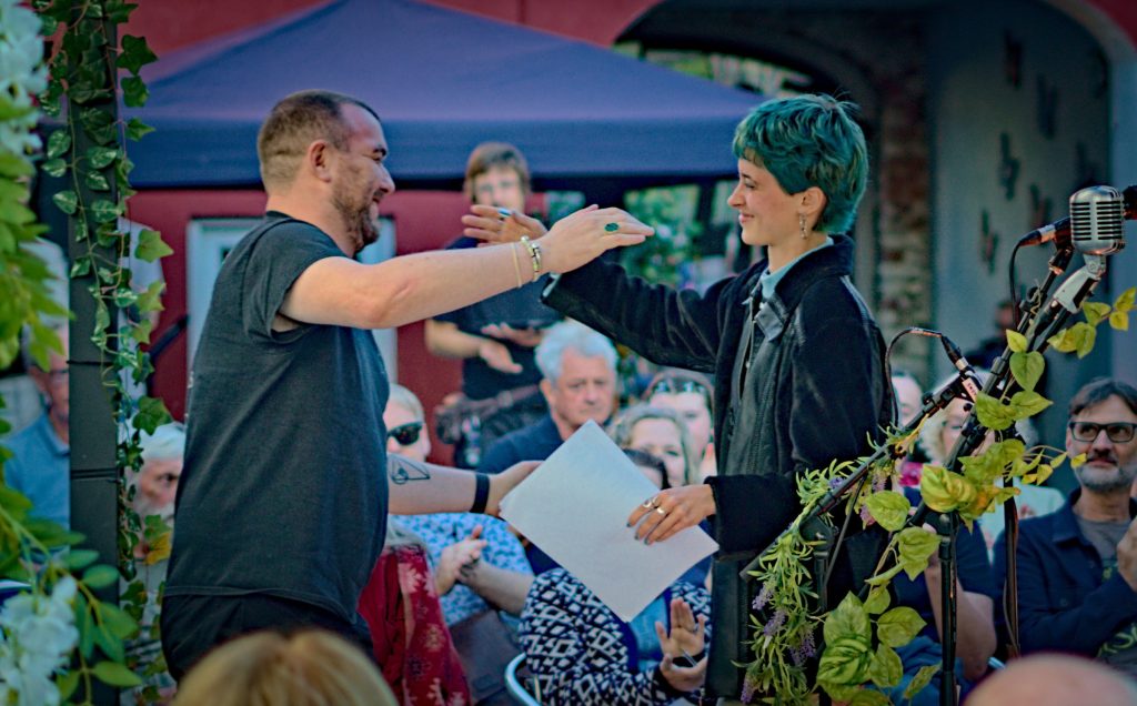 The So Say So host reaching out to Helen of Troy as she leaves the microphone, the audience applauding behind them