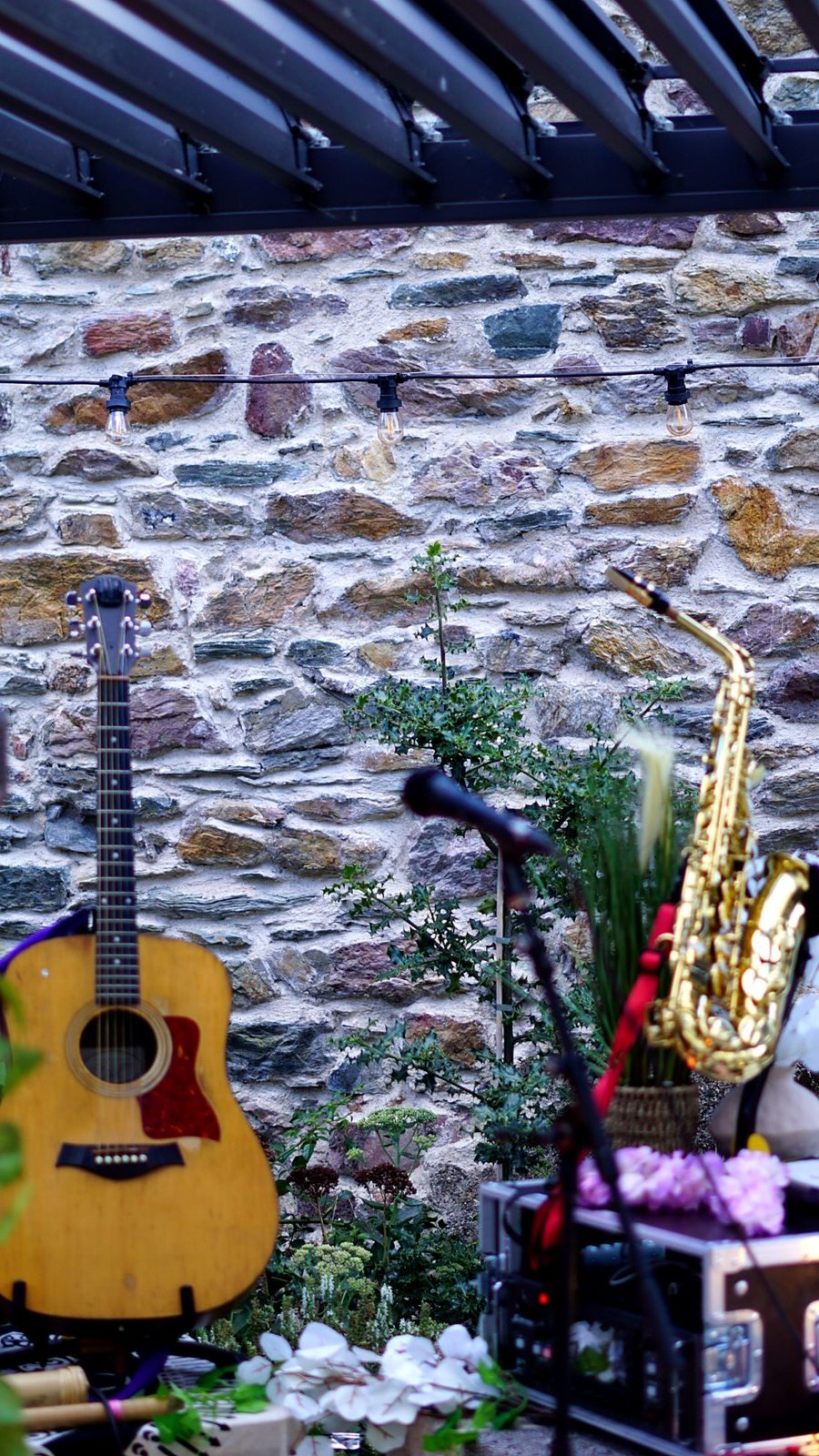 Acoustic guitar and saxophone on stands against the garden's stone wall before the performance